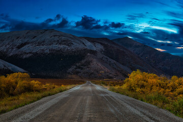 View of Scenic Road and Mountains on a Fall Season in Canadian Nature. Twilight Dramatic Sky Artistic Render. Taken near Tombstone Territorial Park, Yukon, Canada.