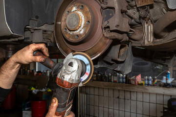 A mechanic grinds, with an angle grinder, the edge of an old rear brake disc in a car, regeneration of the brake system.