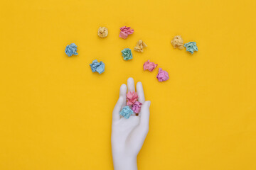 White mannequin hand holding crumpled colored paper balls on yellow background