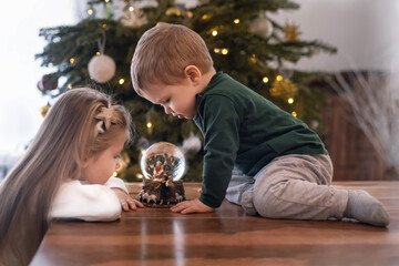 Sister and brother looking at a glass ball with a scene of the birth of Jesus Christ in a glass ball on a Christmas tree