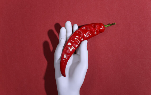 Mannequin Hand Holding Hot Chili Pepper On Red Background