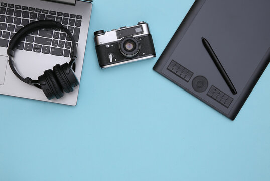 Workspace of a photographer or retoucher. Laptop, graphic tablet, camera and headphones on a blue background. Top view. Copy space