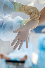 Female assistant putting on protective gloves on hands of professional surgeon