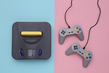 Retro video game console with joysticks on pink blue background. Top view