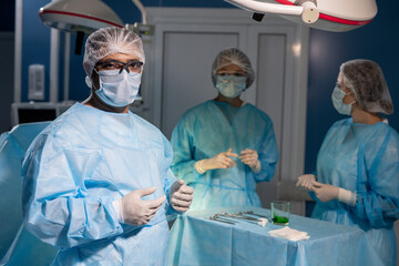 Fototapeta na wymiar Contemporary surgeon in protective mask, gloves and eyeglasses looking at you