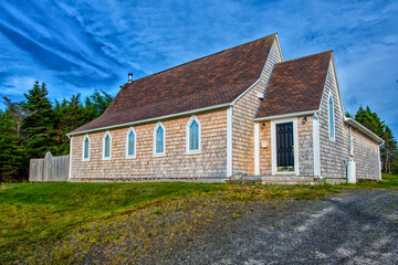 A vintage church recently renovated with cedar shake siding, brown roof shingles and five clear glass steeple clerestory windows. There's green grass in the foreground and blue sky in the background.