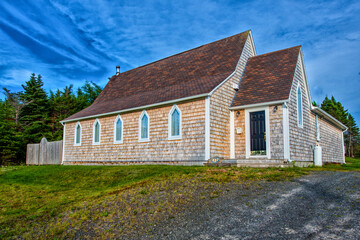 Fototapeta na wymiar A vintage church recently renovated with cedar shake siding, brown roof shingles and five clear glass steeple clerestory windows. There's green grass in the foreground and blue sky in the background.