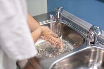 Young assistant or surgeon in white uniform washing hands after operation