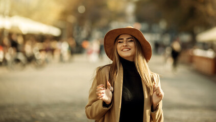 Fototapeta premium Young happy woman dressed in a coat and felt hat walks around the city. Autumn time