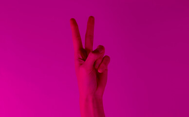 Female hand shows gesture v symbol in pink neon light