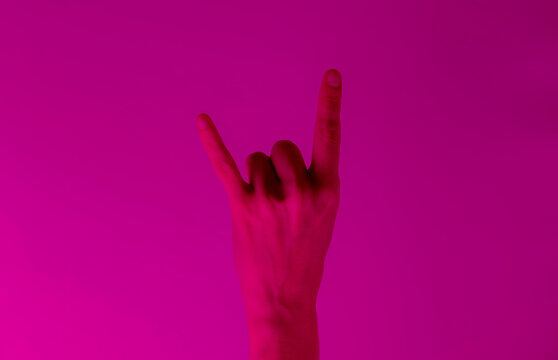 Female hand shows rock gesture in pink neon light