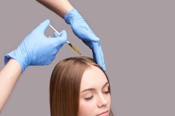 Doctor hands in protective medical gloves. Hair injection. Pretty young woman. Face anti age...