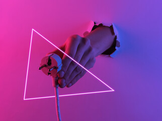 Hand holding electric plug through torn hole. Creative pop art pink blue neon color. Trendy gradient illumination. Night light