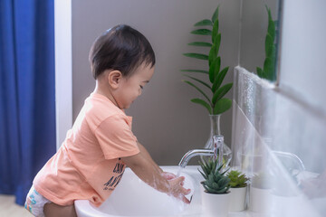 Close-up portrait of baby boy washing hands in bathroom , playing with water, Childhood baby health care and skin care concept.