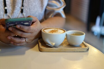 Woman holding a smartphone Sitting on coffee, hot cappuccino with hot tea, relaxation in coffee shop, banner with copy space for text.