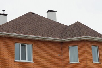 brick house with white windows and brown tiled roof with chimneys against gray sky