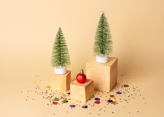 New year creative concept. Two artificial Christmas trees, red Christmas decoration on wooden cubes and multicolored confetti around on a beige background. Christmas background