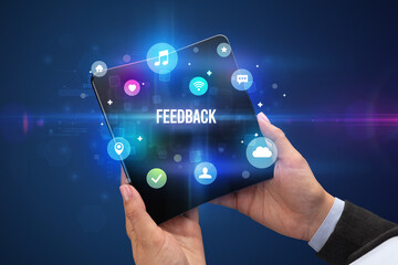 Businessman holding a foldable smartphone with FEEDBACK inscription, social media concept