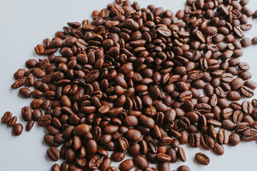Closeup of coffee beans spill out of a glass jar on a light brown background. For coffee houses and coffee shops.