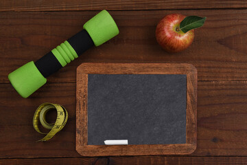 A vintage blank slate chalkboard with apple, dumbbell and tape measure on a rustic wood surface....