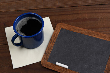 A vintage blank slate chalkboard with a mug of coffee on a rustic wood surface.