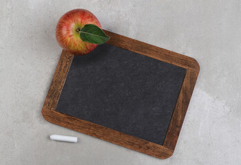 A vintage blank slate chalkboard with an apple on a grey mottled surface. Back to school concept with copy space.
