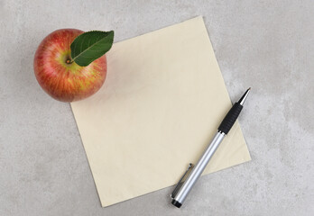 An apple, pen, and napkin on a gray mottled surface. Room for copy or doodle on the napkin.