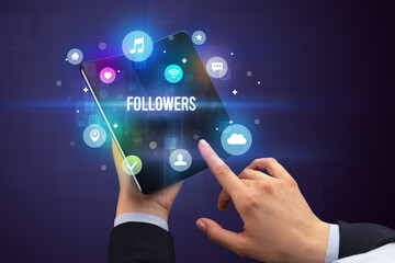 Businessman holding a foldable smartphone with FOLLOWERS inscription, social media concept