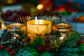 Beautiful new year's holiday candle holder with three candles and lights among green spruce branches and red frosty berries with Golden cones. Warm and cosy decoration