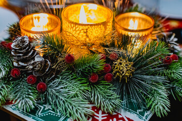 Beautiful new year's holiday candle holder with three candles and lights among green spruce branches and red frosty berries with Golden cones. Warm and cosy decoration
