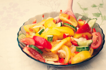 Brown glass plate with salad. Salad of red, yellow tomatoes, green cucumbers, onions.