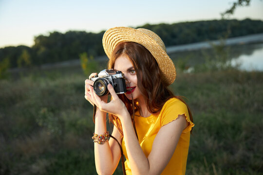 woman photographer looking into the camera lens wearing a hat outdoors takes a picture