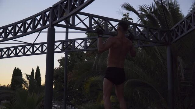 A young man doing back exercises outdoors with a sunset