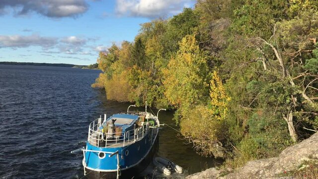 A medium size blue boat with a smaller gray jolly-boat next to it at a Swedish lake called Malaren or Malar. Mostly green forest to the right, early autumn.  Stockholm, Sweden.