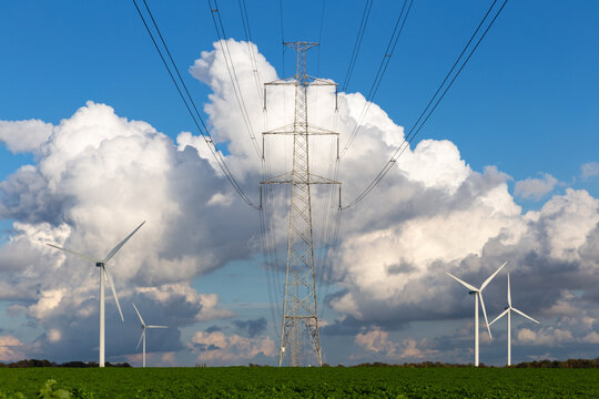 high-voltage power line tower and wind generators in a green field and with a beautiful cloudy blue sky