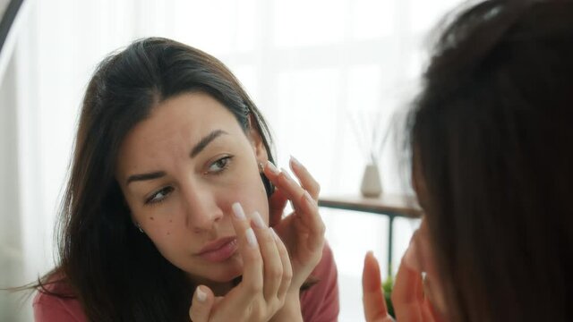 Slow motion of attractive lady removing blackheads from skin looking at mirror in bathroom busy with skincare and checking for imperfections.