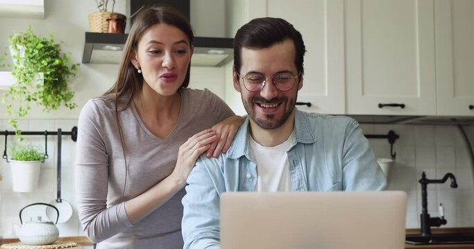 Overjoyed young couple looking at laptop screen, celebrating getting good news notification, banking loan approval, last mortgage payment. Happy spouses supporting favorite team, watching sport match.