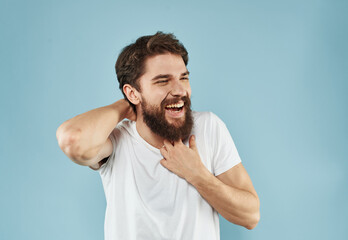 Cheerful guy in a T-shirt with a beard on a blue background holds his hand behind his head