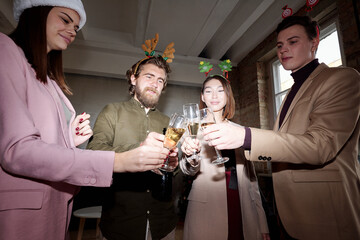 Young contemporary managers clinking with flutes of champagne on Christmas day