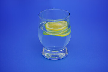 Sliced lemon in a glass of water on an isolated blue background.