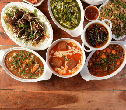 Assorted Indian Food On Wooden Background. Dishes And Appetizers Of Indian Cuisine. Tomato Soup, Veg Manchurian Balls, Dal Tadka, Paneer Butter Masala, Palak Paneer, Veg Fried Rice