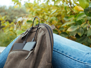 The phone is charged using a power Bank. Use of modern technologies in everyday life. The phone and powerBank are in the tourist's leather backpack. Convenient modern gadgets for a comfortable life