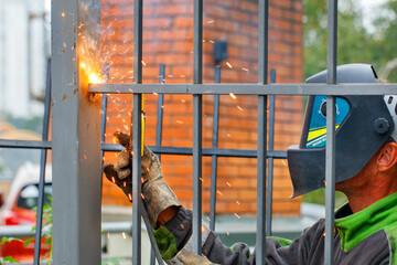 A welder wearing a protective helmet and gloves is welding a metal fence around an apartment building.