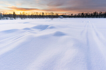 Naklejka premium Winter sunset in Finnish Lapland with log cabin and forest in the background, deep snow in the foreground. Picture taken in Pyha, Finland.