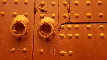 old wooden studded double doors in golden brown paint in Marrakesh Morocco, with original antique door knobs and key holes