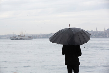 Man standing by the sea with black umbrella on a rainy day