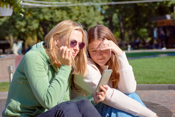 Two young girls friends using smartphone outdoors on the street. Lifestyle and friendship concept