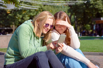Girls watching videos on a smartphone and pointing at screen surprised - Girlfriends laughing and having fun outdoors