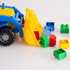 Closeup of a brightly colored tractor with multi-colored bricks on a white table. Development concept