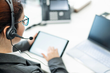 A business woman with a headset holds a digital tablet while sitting at a desk